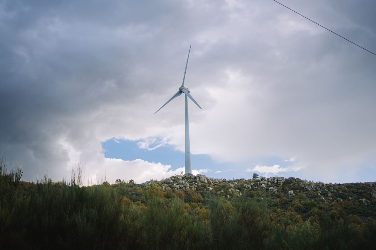 A wind turbine stands on a hill against a dramatic cloudy sky, symbolizing renewable energy.