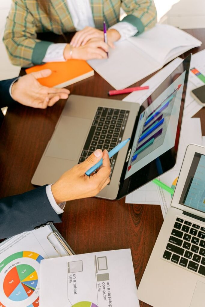 Ingeniería técnica, licencias y subvenciones | ALD Serveis d'Enginyeria A productive workspace with colleagues discussing data charts and using laptops for business collaboration.
