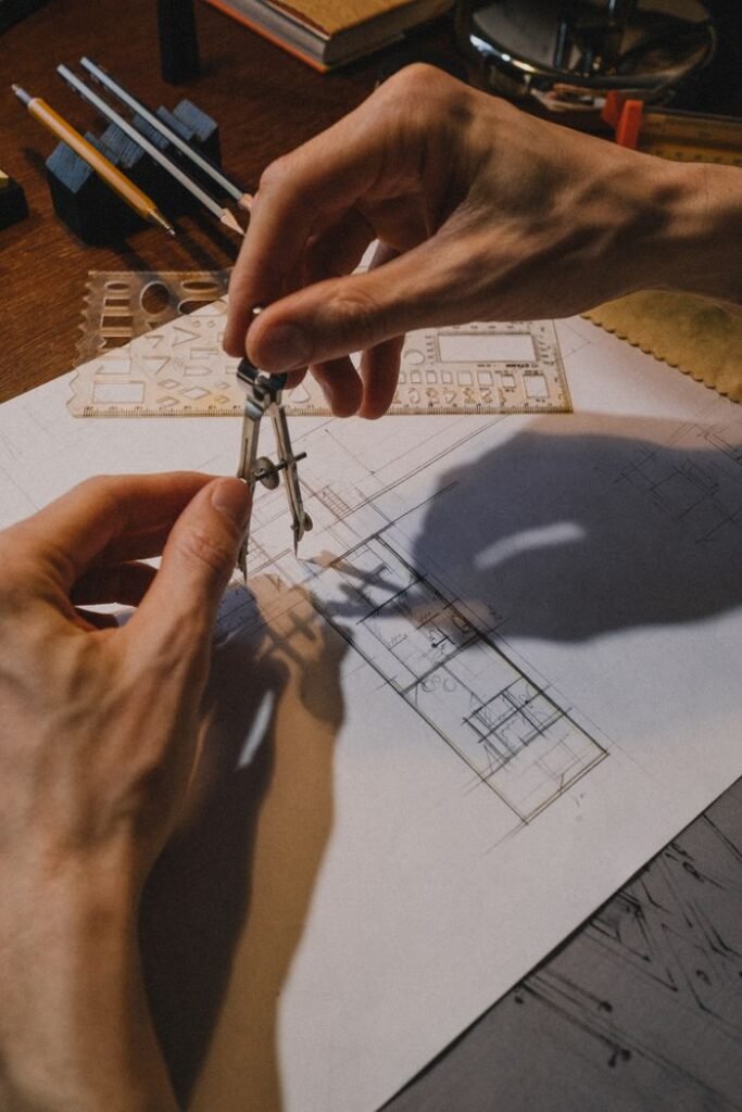 Ingeniería técnica, licencias y subvenciones | ALD Serveis d'Enginyeria Detailed shot of hands using a compass on an architectural blueprint with drafting tools.